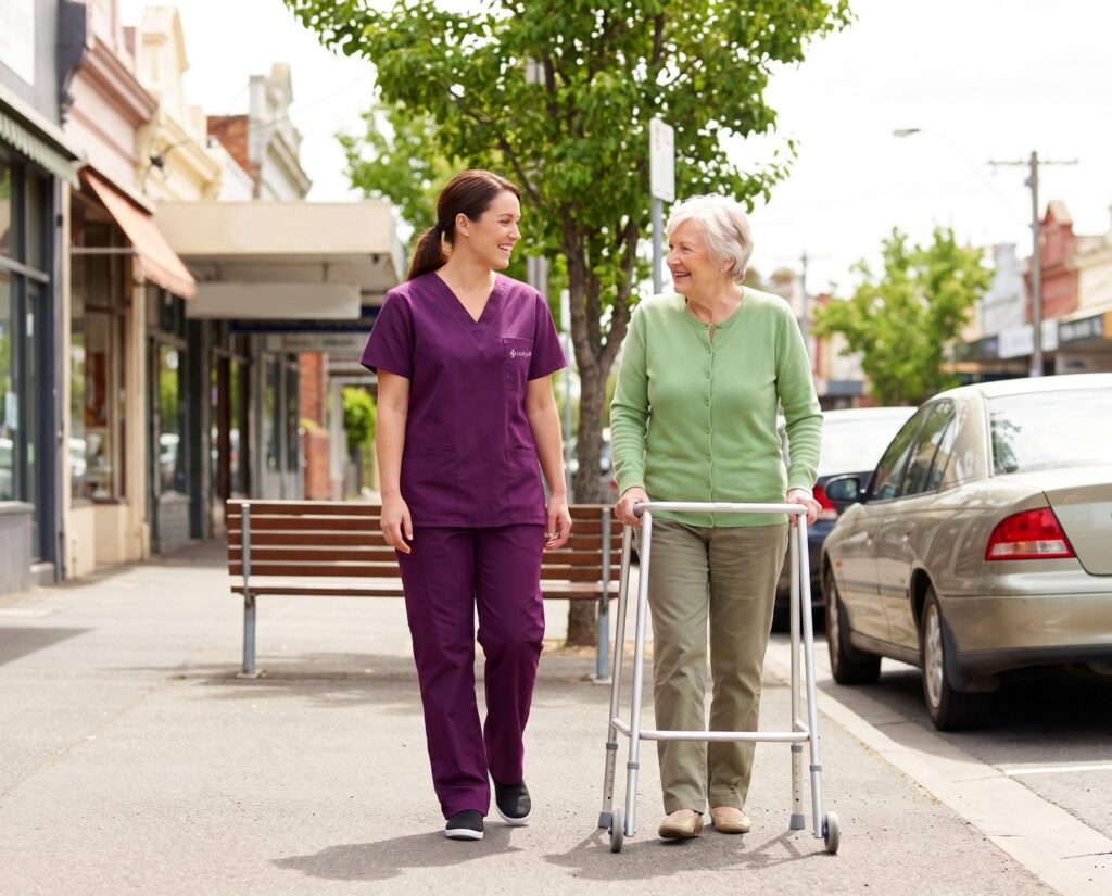 A support worker and an older woman walking along a suburban shopping strip.