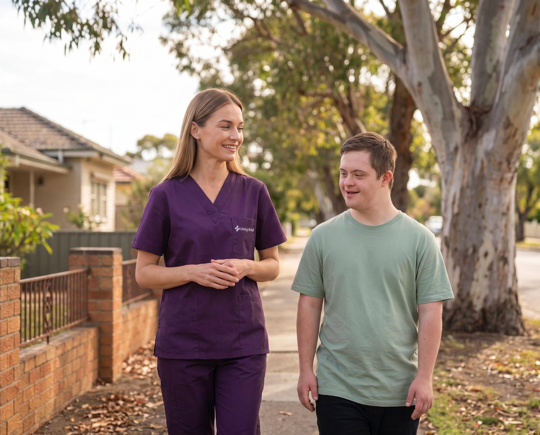 A support worker and a young man walking together along a suburban street.